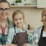 Portrait of adorable little girl, young mother and mature grandmother wearing aprons smiling in kitchen at home. People , cookery and apartment concept.