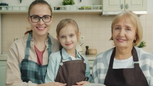 Portrait of adorable little girl, young mother and mature grandmother wearing aprons smiling in kitchen at home. People , cookery and apartment concept.