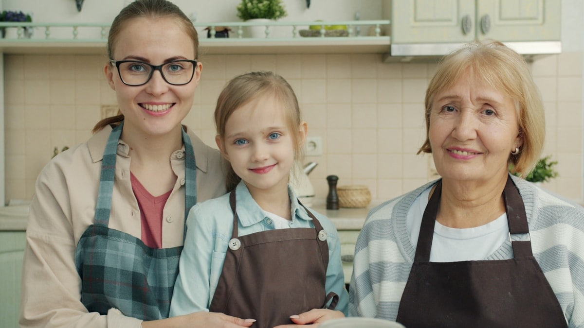 Portrait of adorable little girl, young mother and mature grandmother wearing aprons smiling in kitchen at home. People , cookery and apartment concept.